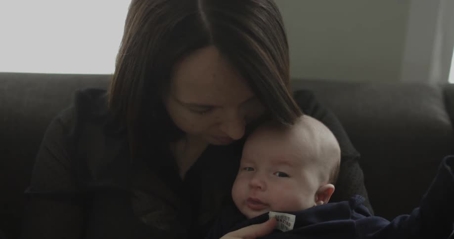 A woman is holding a baby as she sits on a couch