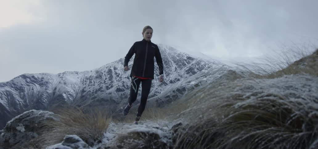 A woman is jogging up a snow-covered hillside
