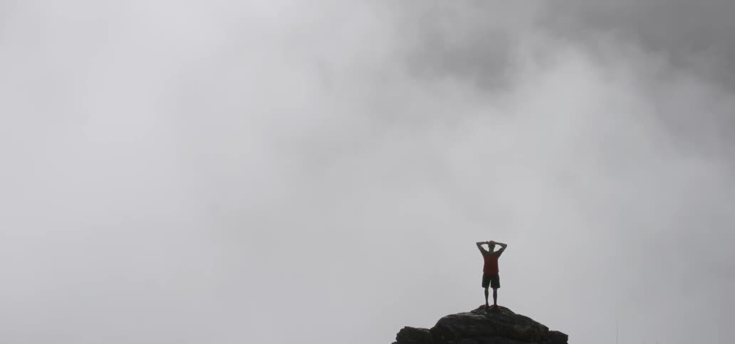 Man standing with arms over his head at the edge of a cliff