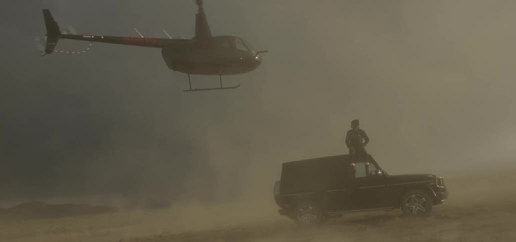 A man is sitting on his truck looking up at a helicopter