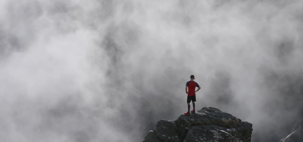 Man stands on a cliff looking into the fog