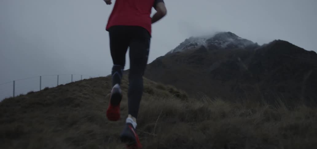 A man is jogging toward the peak of a fog-covered mountain with snow on it