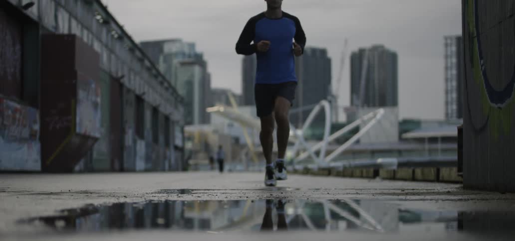 A man jogs on a city sidewalk with a puddle on the ground
