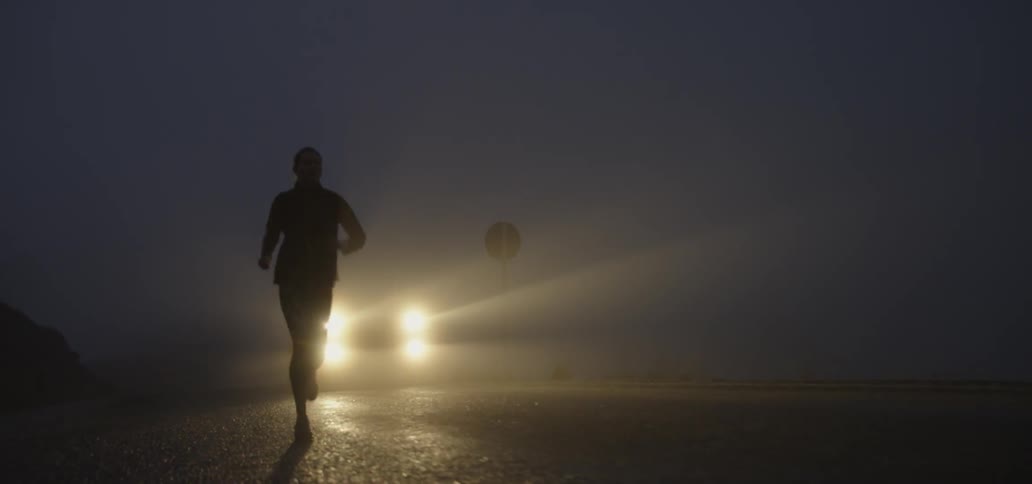 Person jogs outside at night followed by headlights