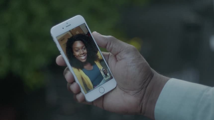 Hand holding a phone showing a laughing woman waving