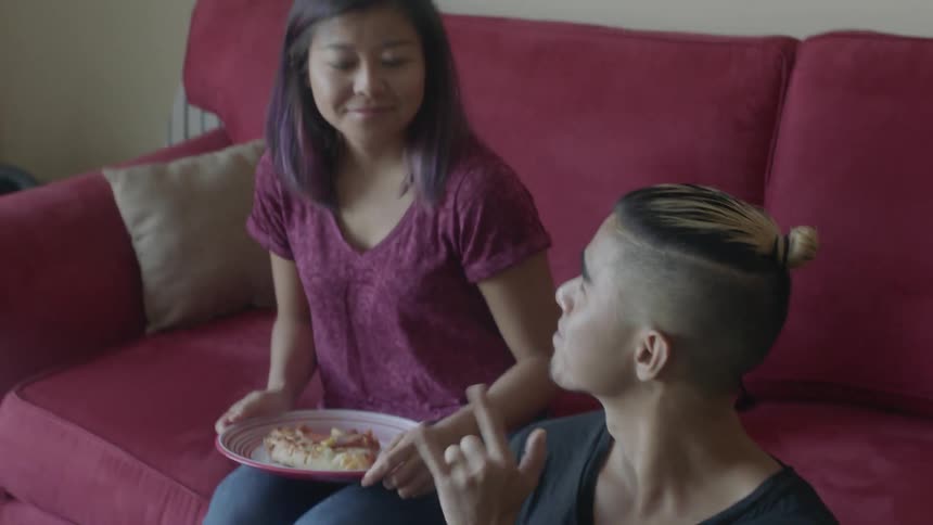 A woman sits down to eat next to a man using a laptop
