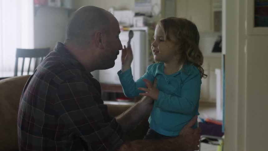 A man plays with a small girl on a living room couch