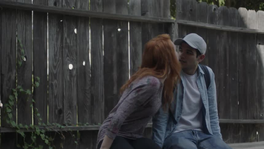 A woman kisses a man as they sit outside