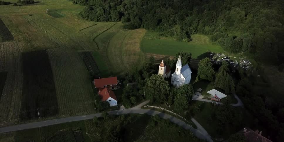 A church sits surrounded by a copse of trees and other buildings in a quaint village