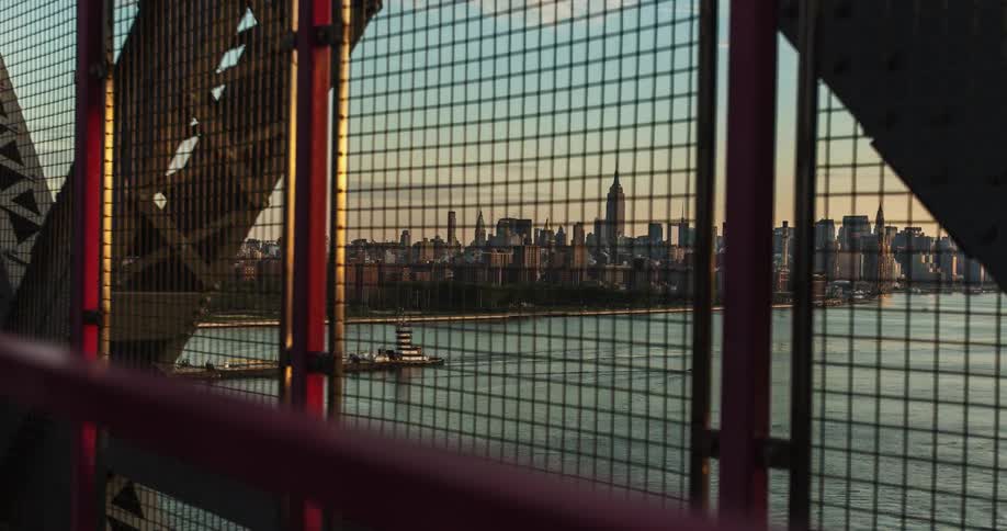 A fence is on this bridge with a city seen in the distance