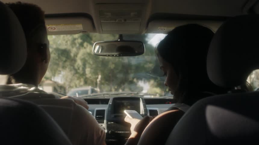 A man drives as a woman checks her phone