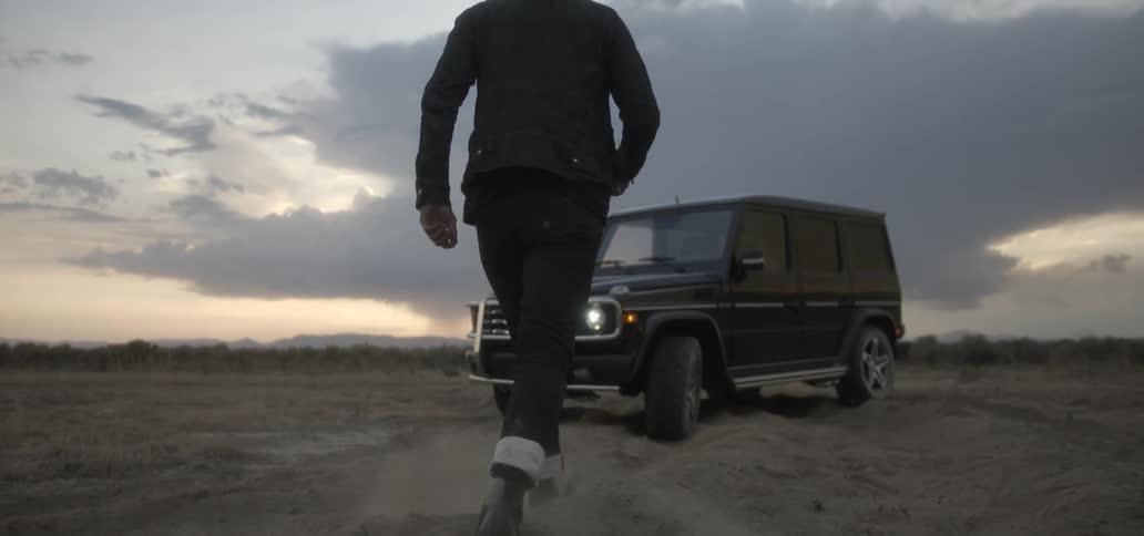 A man walks through a dirt field towards a vehicle at sunset