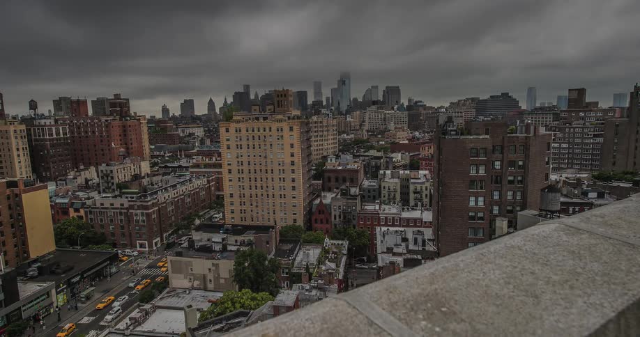 Cars drive on a city road as dark clouds pass overhead