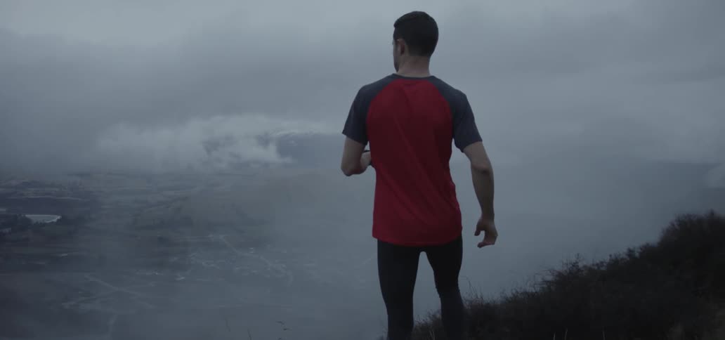 A man jogs up to the edge of a cliff and then stops to take in the view