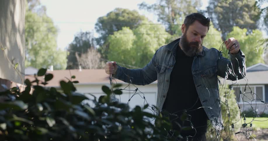 A man sets up christmas lights in the front yard
