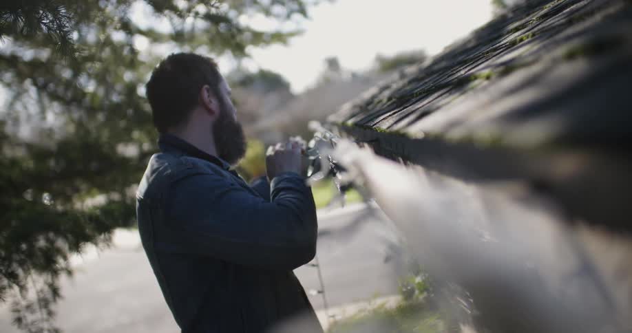 A man is putting christmas lights on his roof
