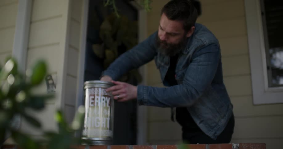 A man is adjusting a candle in a christmas lantern on his porch