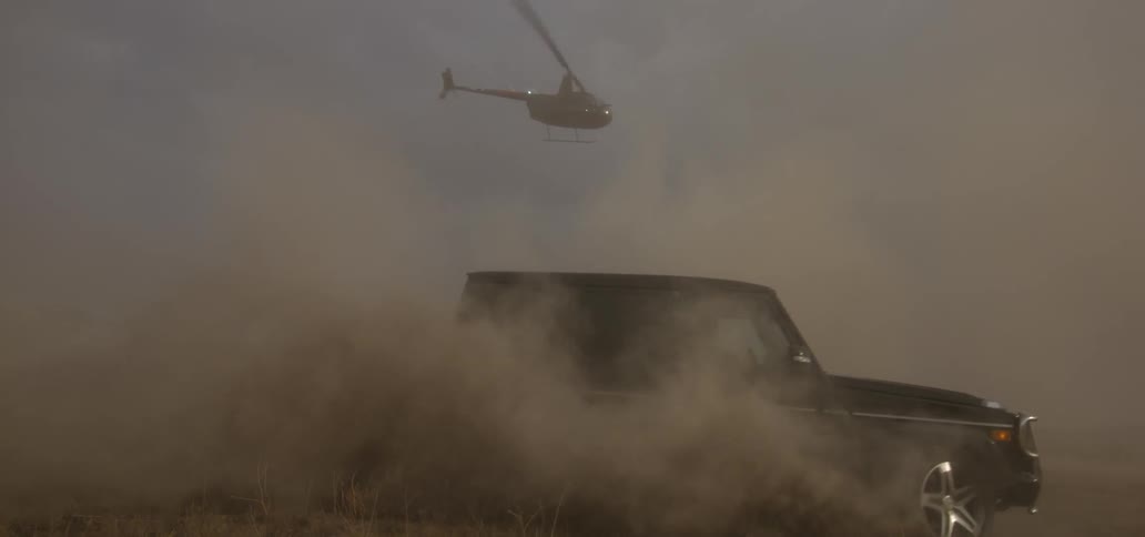 A helicopter hovers over an suv that is making a tight turn