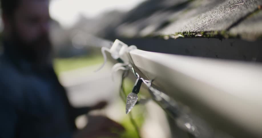 A man hangs lights on his roof gutter
