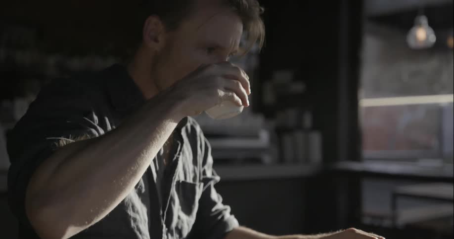 A man takes a drink from his coffee as he works at a laptop in a cafe