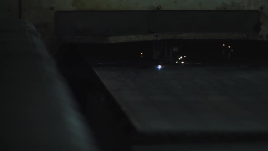 Sparks fly from an industrial laser cutter as it cuts a sheet of metal