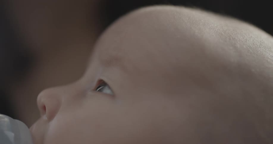 A baby is sucking on a bottle and looking around