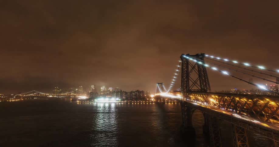 Cars and boats travel around and on a bridge at night