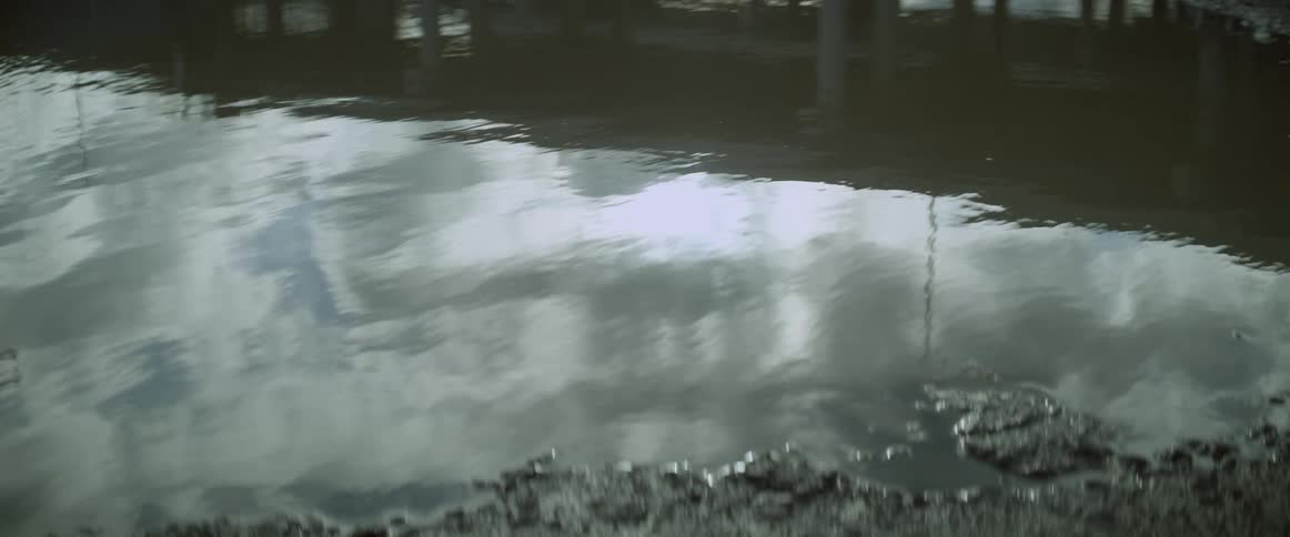 Lake water ripples and reflects a pier and the cloudy sky