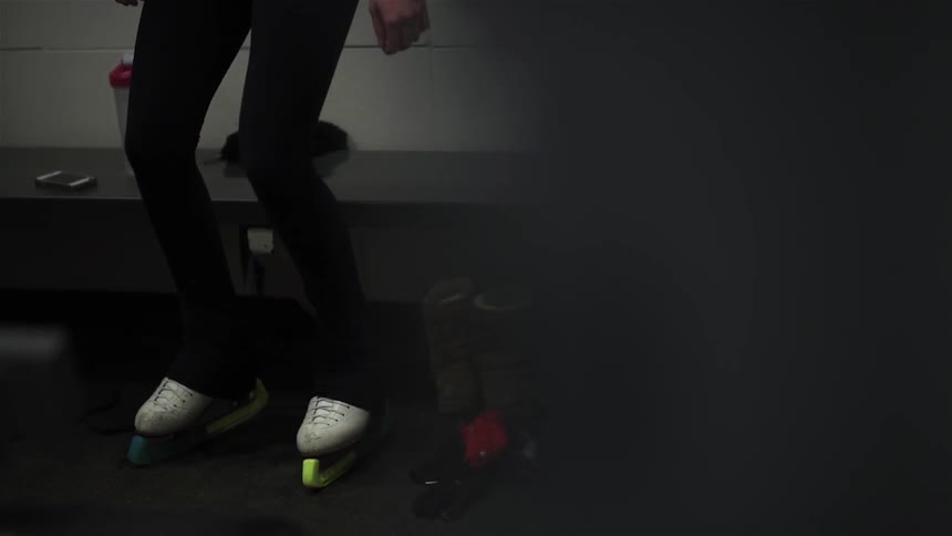 A woman wearing ice-skates is warming up and stretching
