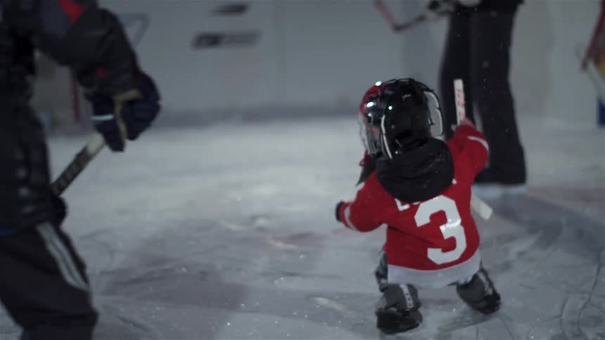 A toddler in a hockey uniform takes a tumble on the ice