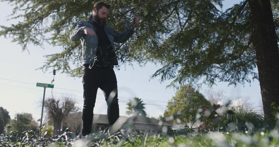 A man is untangling a string of lights as he stands in his yard