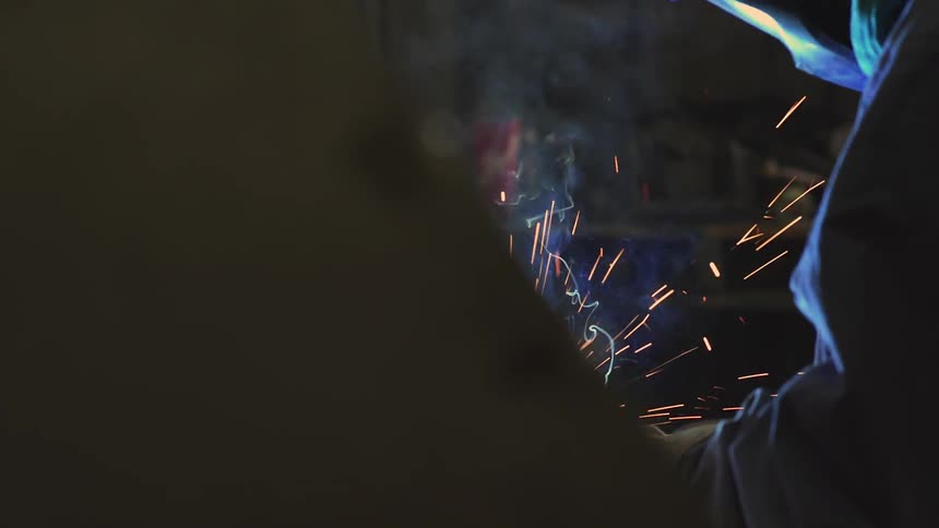 Sparks fly around a welder in a mask
