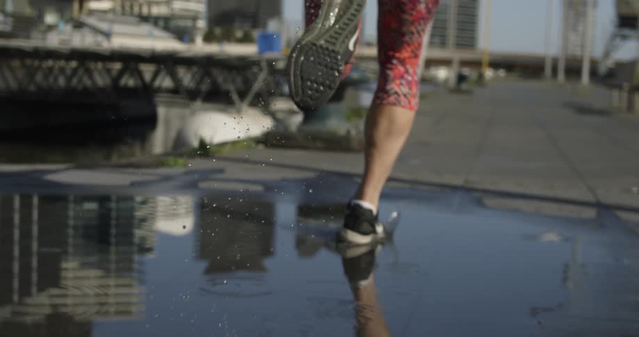 A female jogger runs through a puddle on a path near an urban waterway