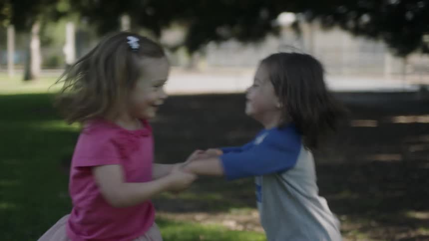 A boy and girl hold hands and spin around in a park