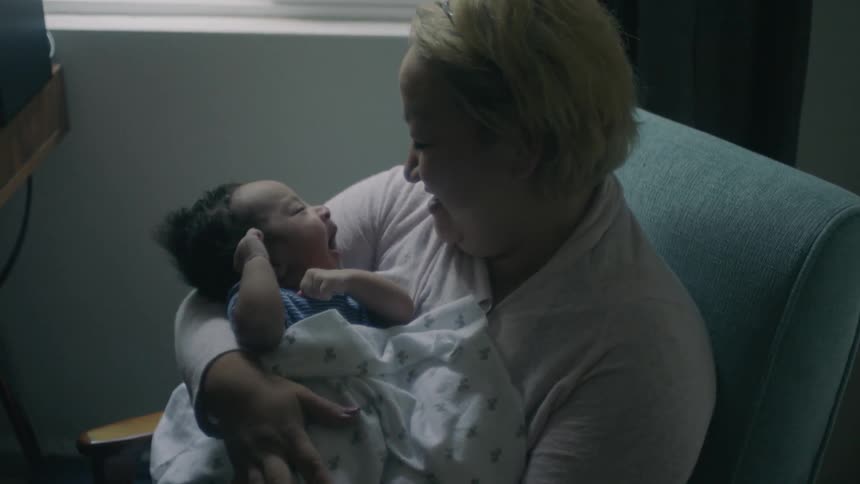 Woman smiles and holds a baby sitting in a chair