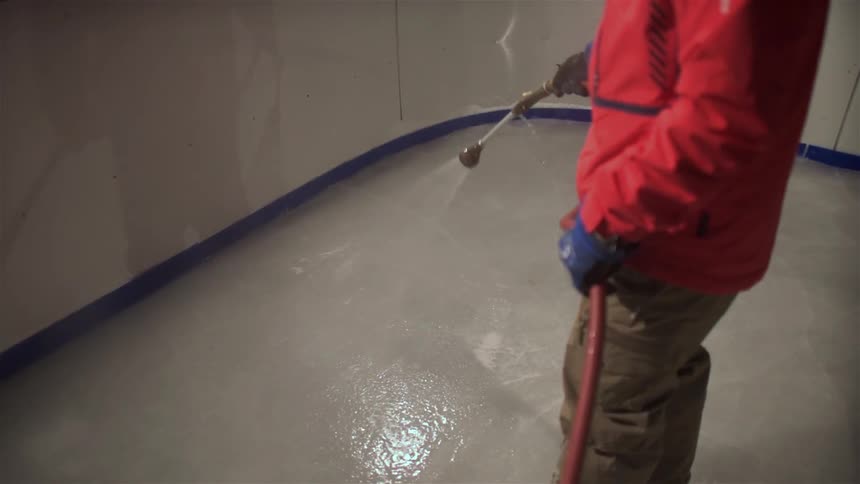 A worker is spraying water onto the ice in an ice-rink