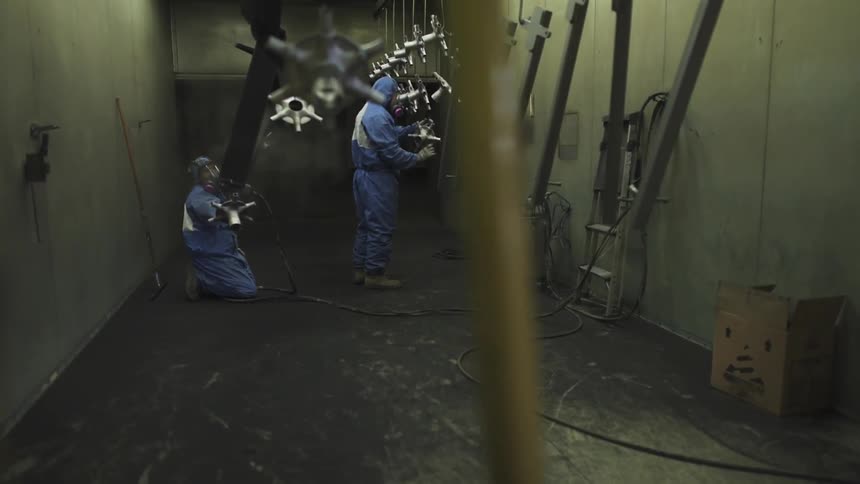 Two men in protective clothing are working hanging parts in a room