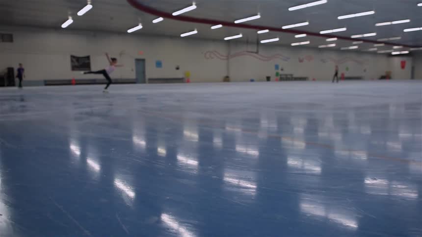 An ice skater is doing jumps on the rink