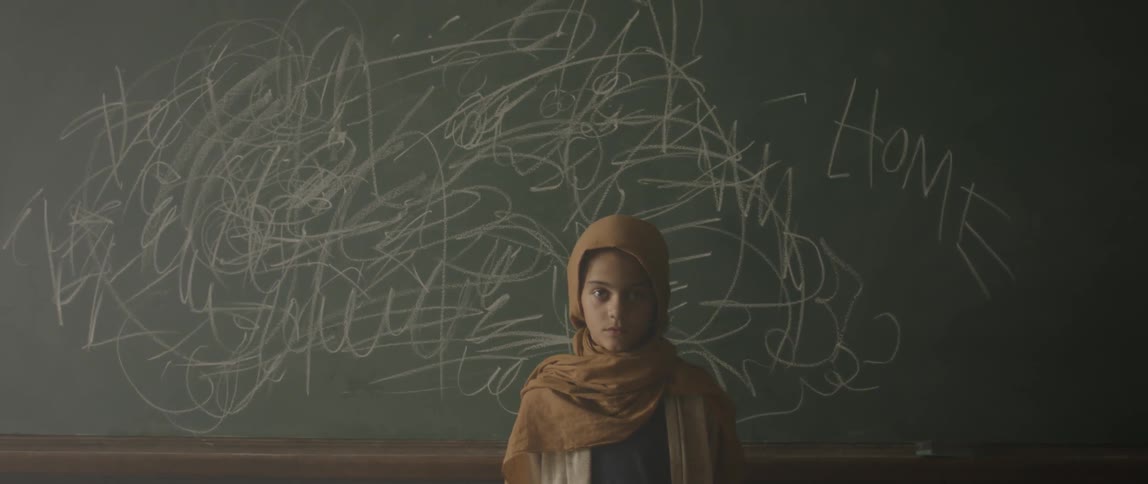 Girl standing in front of a classroom chalkboard that has scribbling all over it
