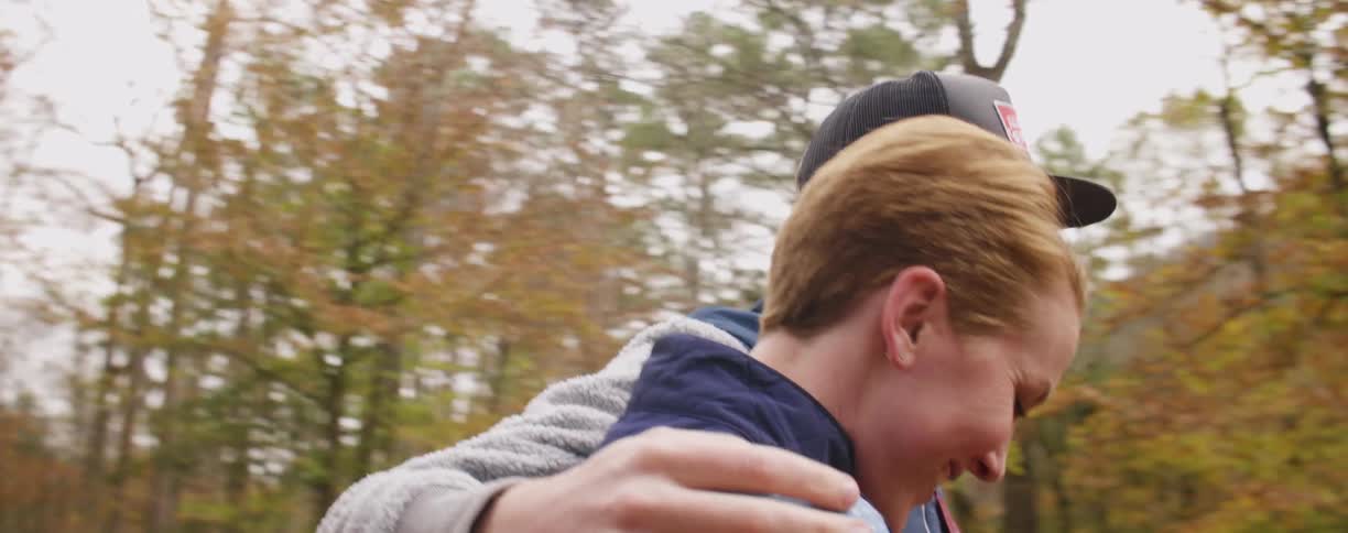 A man and woman hug and talk as they walk towards the woods