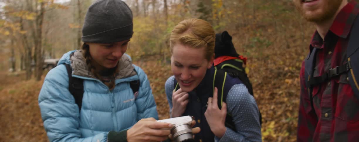 Three people look at photos on a camera and talk