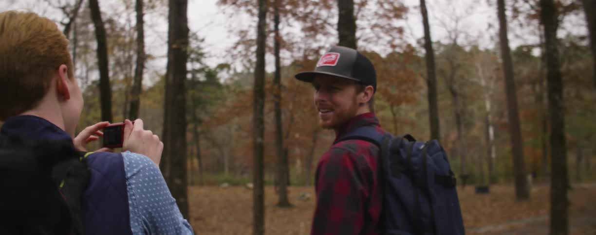 A woman films a man as they hike in the woods