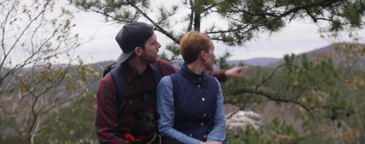 Man and woman sit together outside in the woods smiling