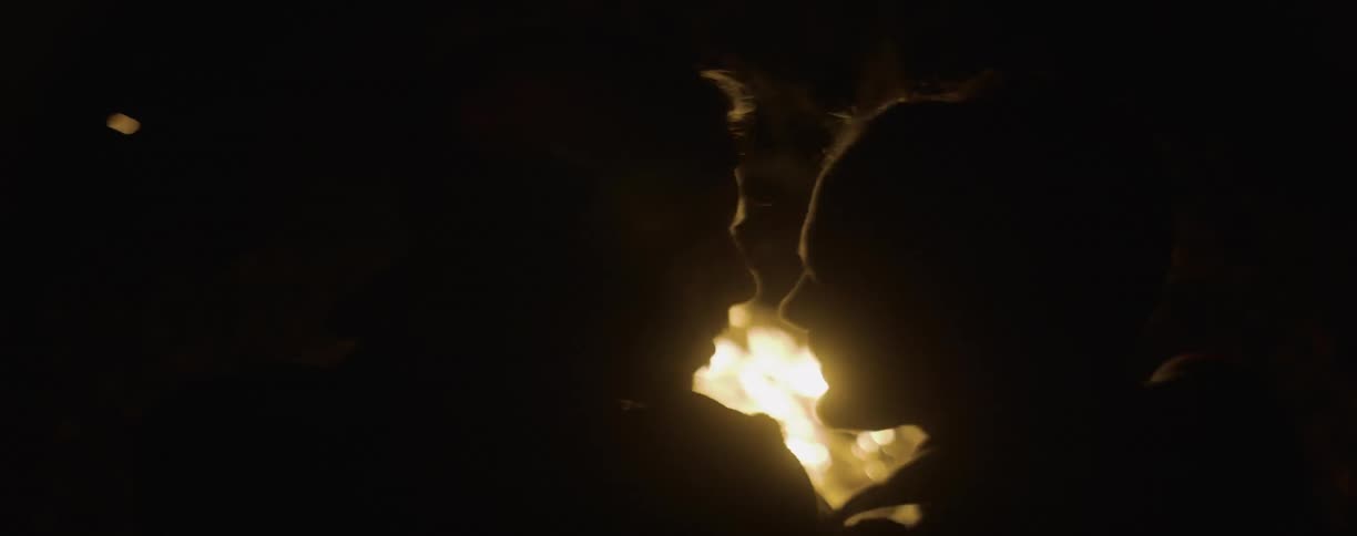 Man and woman sitting close talking in front of a fire