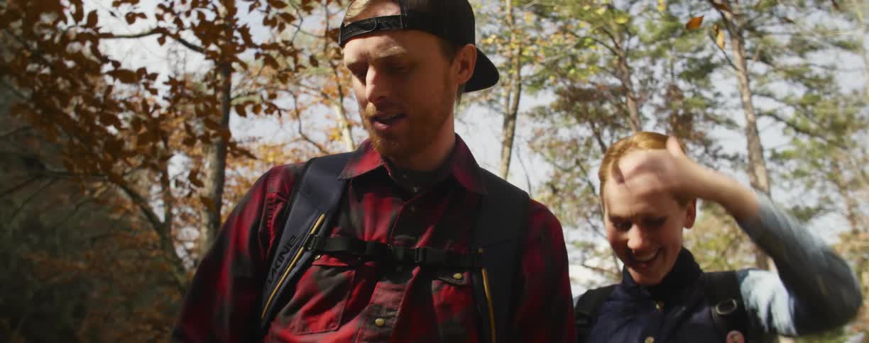A hiking couple smile as they move to take a seat on a log
