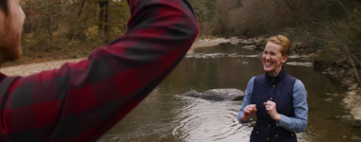 A woman skips a rock across the water and high fives a man