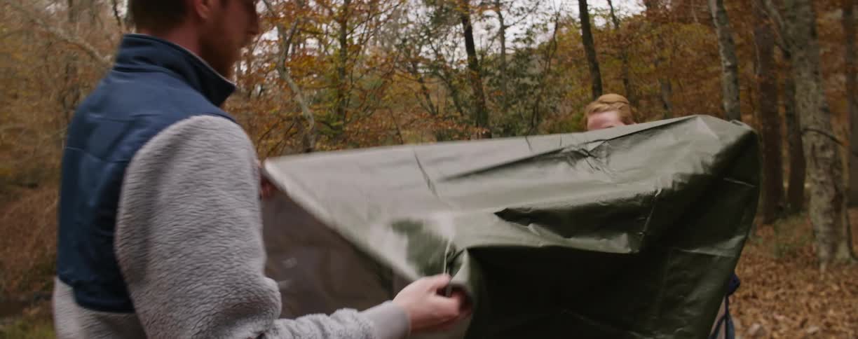 Man and woman unfold a piece of canvas together in the woods