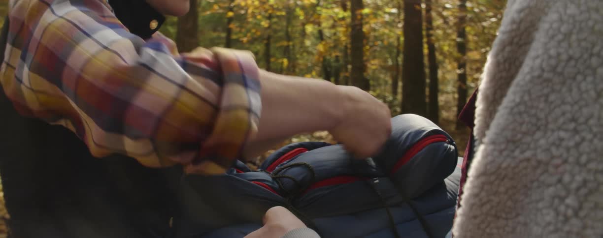 Man and woman tie a sleeping bag together in the woods