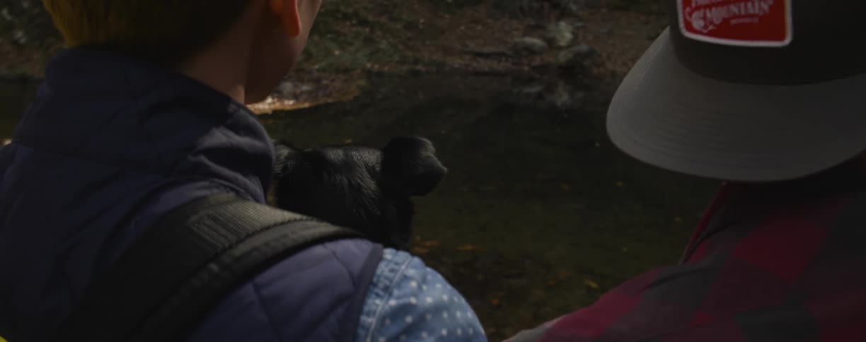 Two people sitting outside petting a black dog