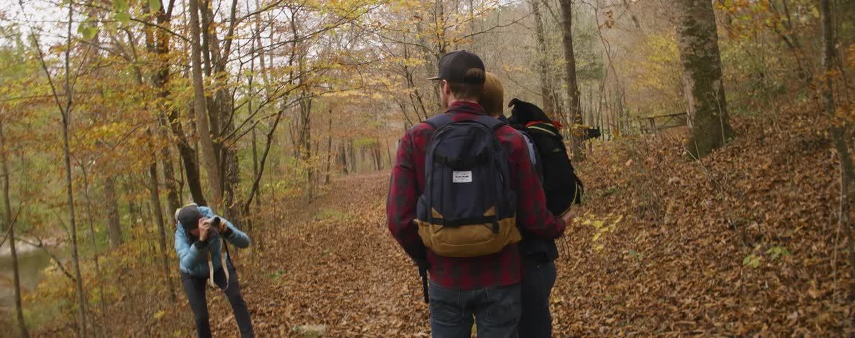 Woman takes picture of two men and a dog in the woods